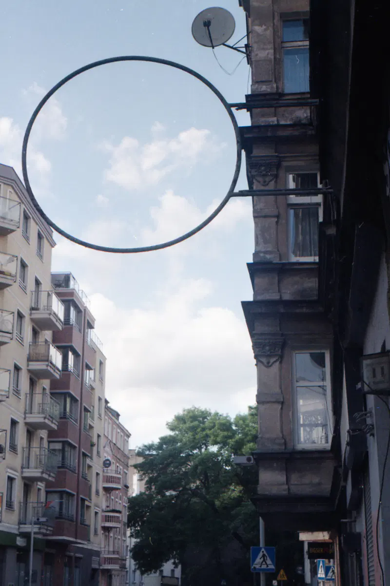 blick in eine straßenschlucht zum himmel, rechts und links mehrfamilienhäuser und als clou ein kreisförmiger, leerer rahmen eines werbeschilds, der ins ganze bild hinein ragt.