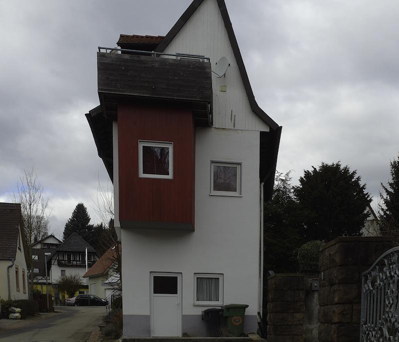 Ein älteres schmales Haus von der Seite fotografiert. Man sie einen zusätzliche Raum der mit Holz mit einem roten Anstrich an das 1. Obergeschoss dran montiert wurde. Zusätzlich ist darauf noch ein Balkon aus Holz oben dran montiert. Schwer vorstellbar, das dafür eine Genehmigung vorliegt.