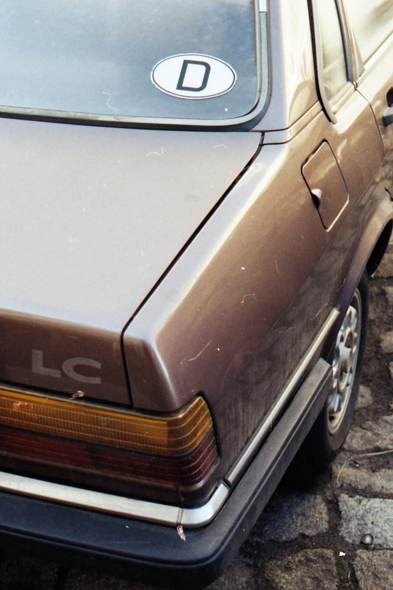 detail eines älteren autos, von schräg oben das heck des braun lackierten fahrzeugs, auf der heckscheibe ein D-Aufkleber