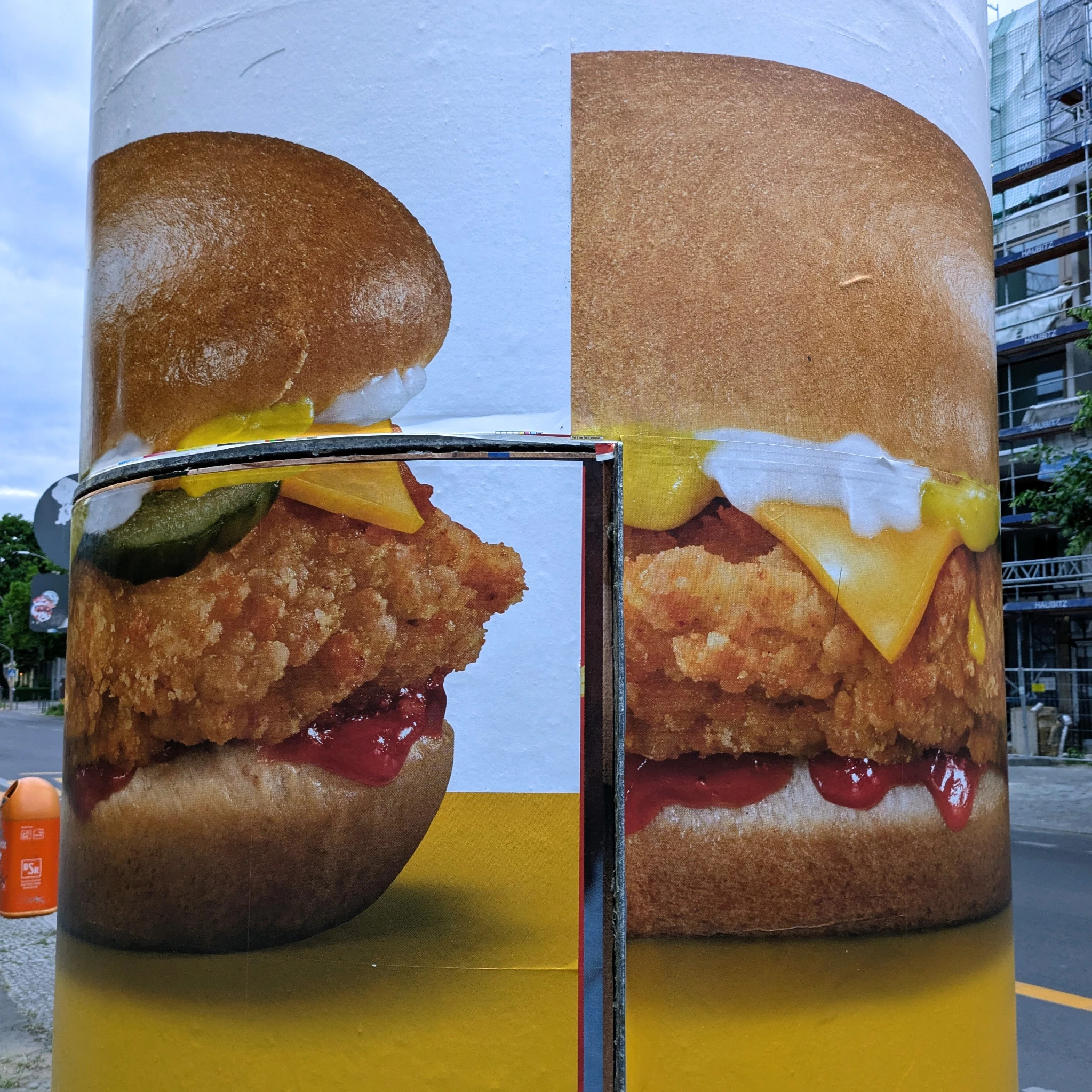detail einer Litfaßsäule, ein werbeplakat für hamburger ist nicht bündig geklebt, sieht etwas wild aus