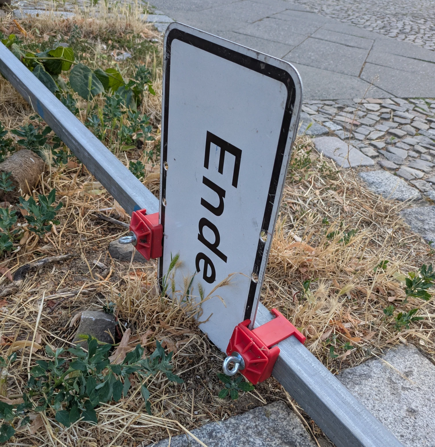 auf einem vertrockneten stück rasenfläche zwischen borsdsteinpflaster liegt ein umgekipptes verkehrsschild, auf dem nur "Ende" steht
