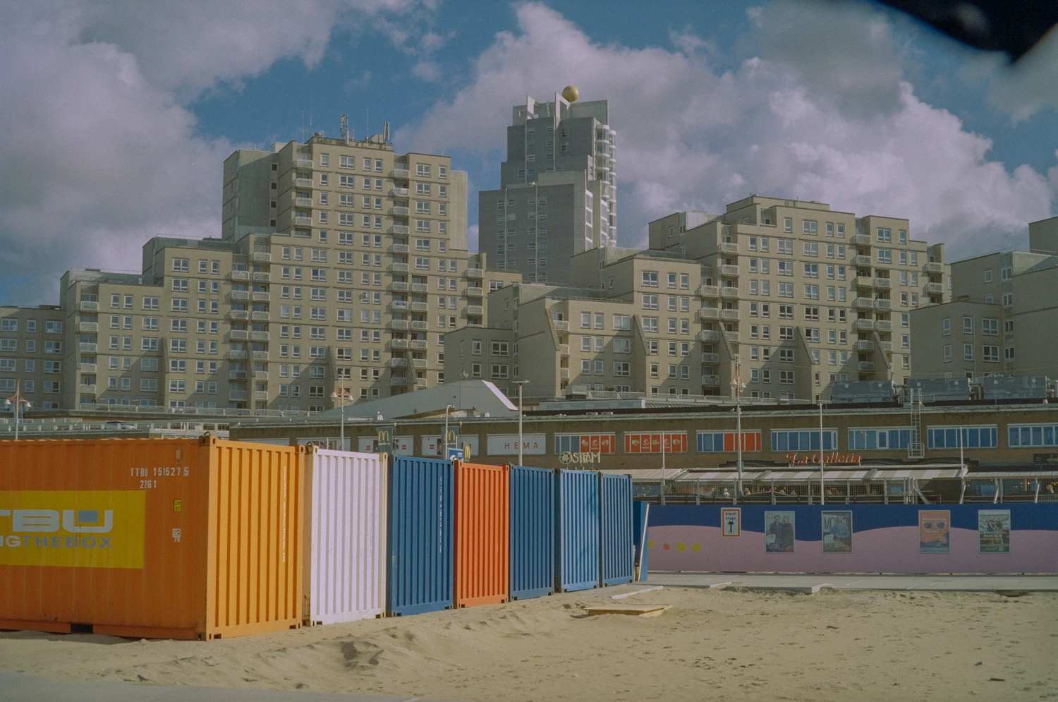 looking from the beach to huge buildings in the background. blue sky with some clouds, colorful containers in the foreground