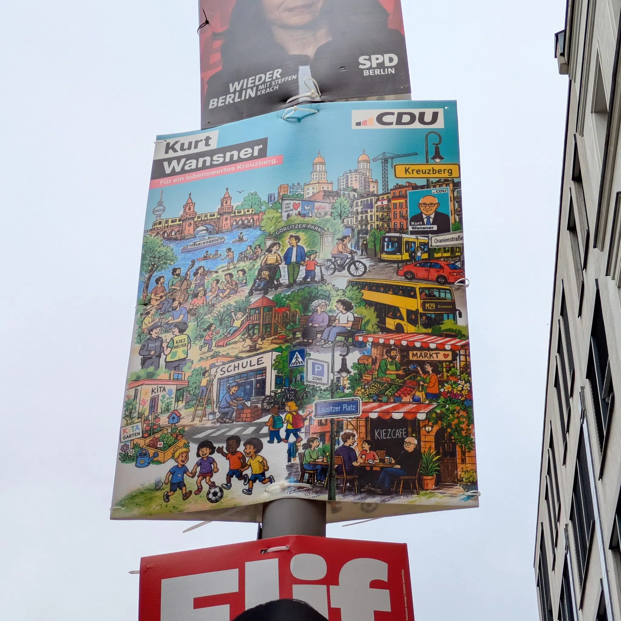 bild einer laterne mit drei wahlplakaten, nur das mittlere ist komplett drauf, ein wimmelbild mit viel frohsinn