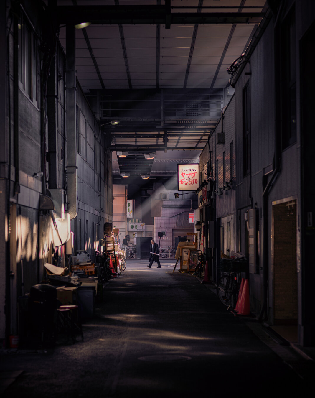 I don't do so much street photography at the moment. But this alleay way has been a favourite for years. It's next to the underneath of the railway tracks and there's a highway overhead nearby too. We see a man walking past the end of the alleyway. The backs of various restaurants. Smoke coming out of one is picking up rays of sun coming through from above.